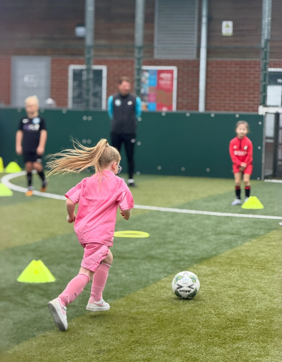 Young girl dribbling through cones at a Bournemouth Ballers girls-only football camp at Pelhams Park, Bournemouth